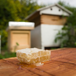 Natural cut comb honey from Leicestershire placed on a wooden board. You can see a couple of lovely beehives in the background